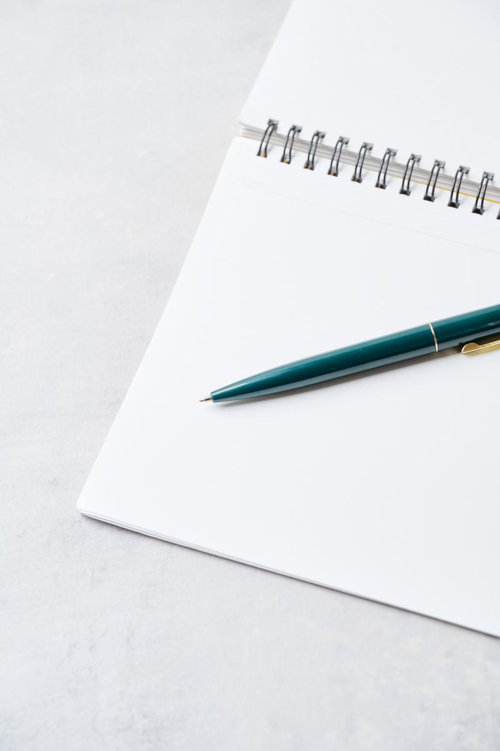 白紙のスパイラルノートとグリーンのボールペン