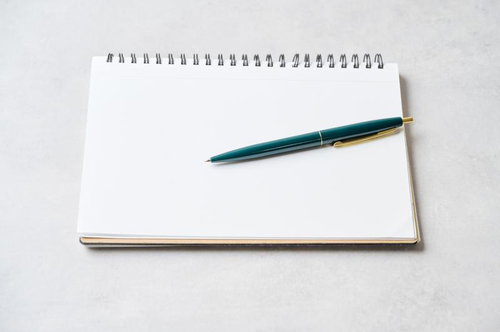 開いたスパイラルノートに置いたトルコ青のボールペン