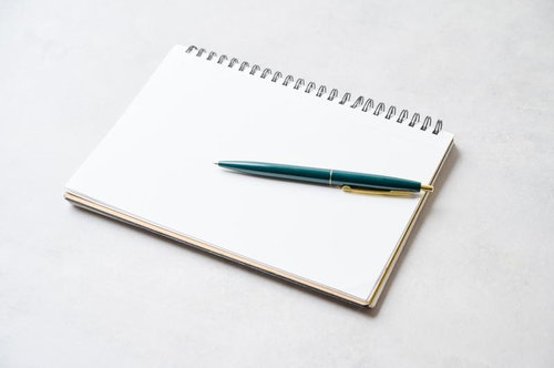 白いスパイラルノートに置かれた緑色のボールペン