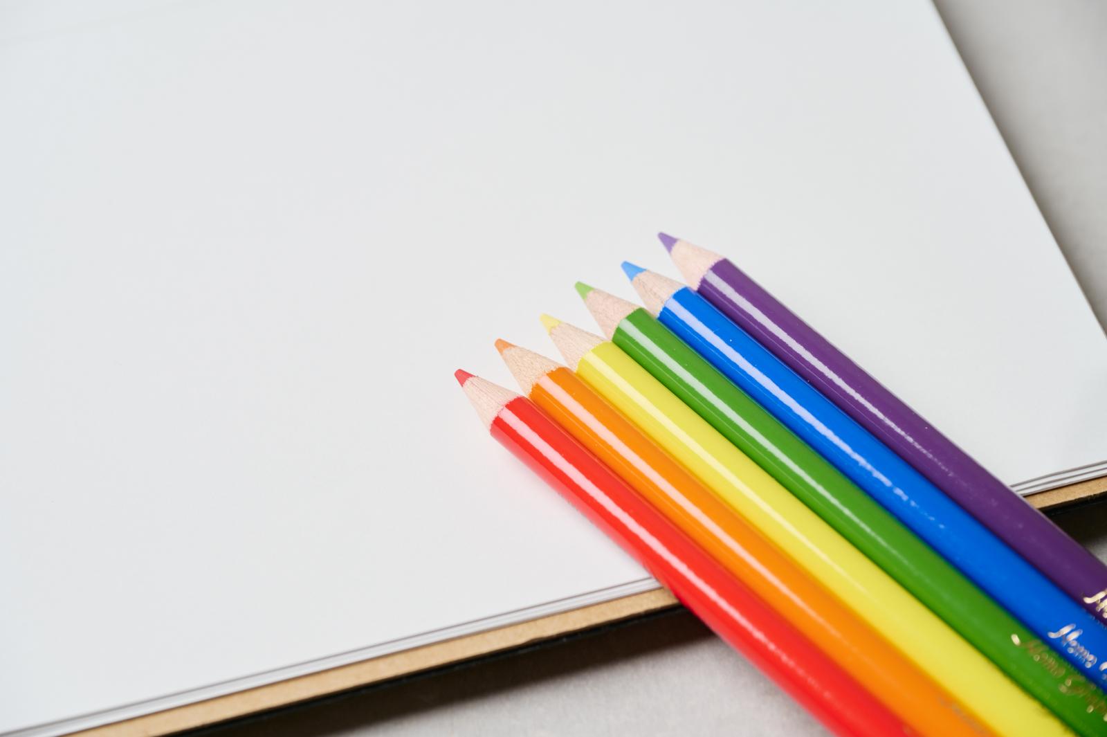 白いノートの上に虹色に並べられた色鉛筆6本