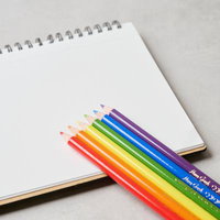 白いスパイラルノートに並んだ虹色の色鉛筆の写真