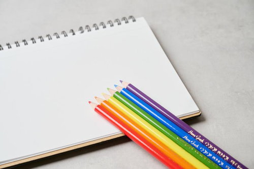 白いスパイラルノートに並んだ虹色の色鉛筆