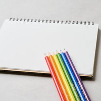白いスケッチブックに並べた虹色の色鉛筆と描画道具の写真