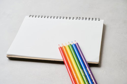 白いスケッチブックに並べた虹色の色鉛筆と描画道具