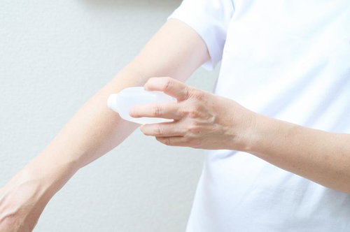 白いシャツを着た人物が腕にローションを塗る