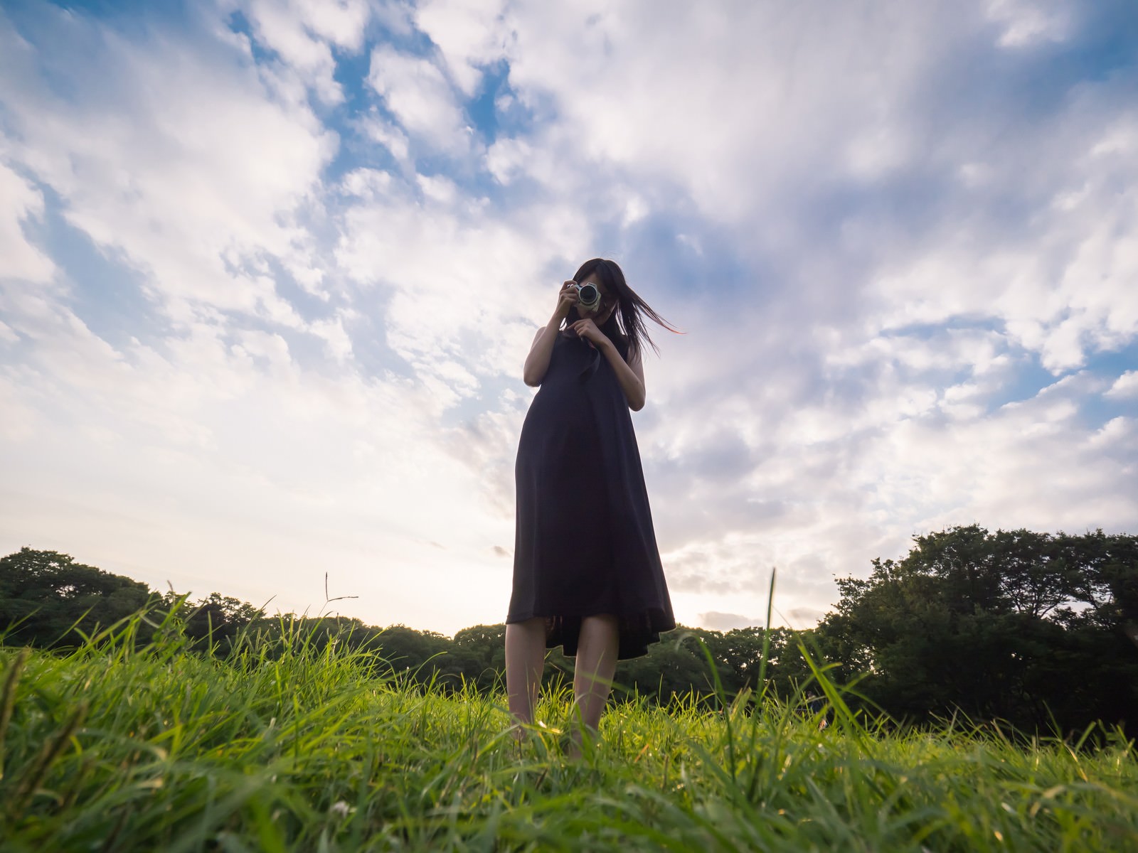草原で一眼レフを構える黒いワンピースの女性