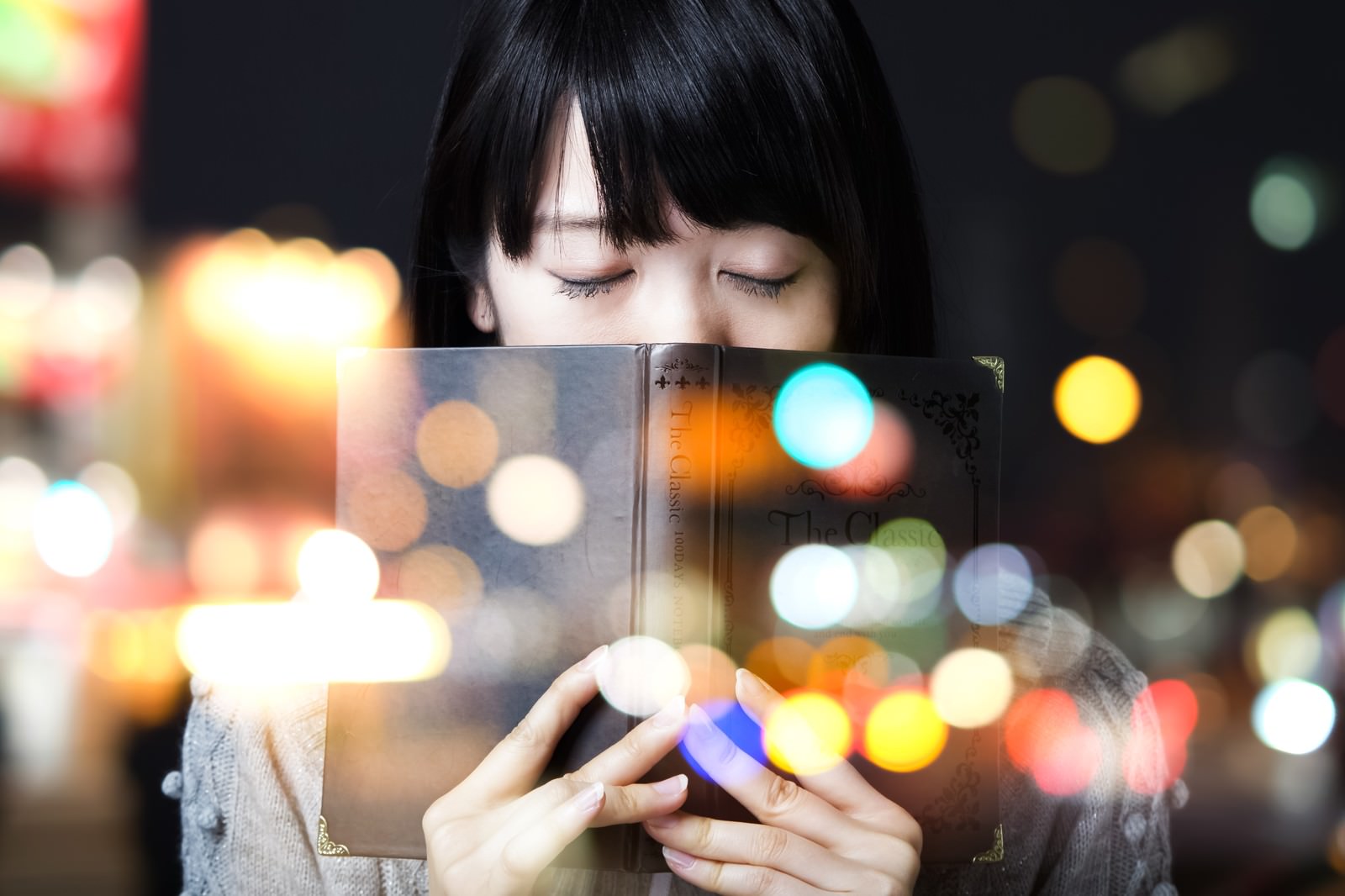 洋書を持ち目を閉じる女性と、背景に光る丸ボケ［モデル：モデルリリース］