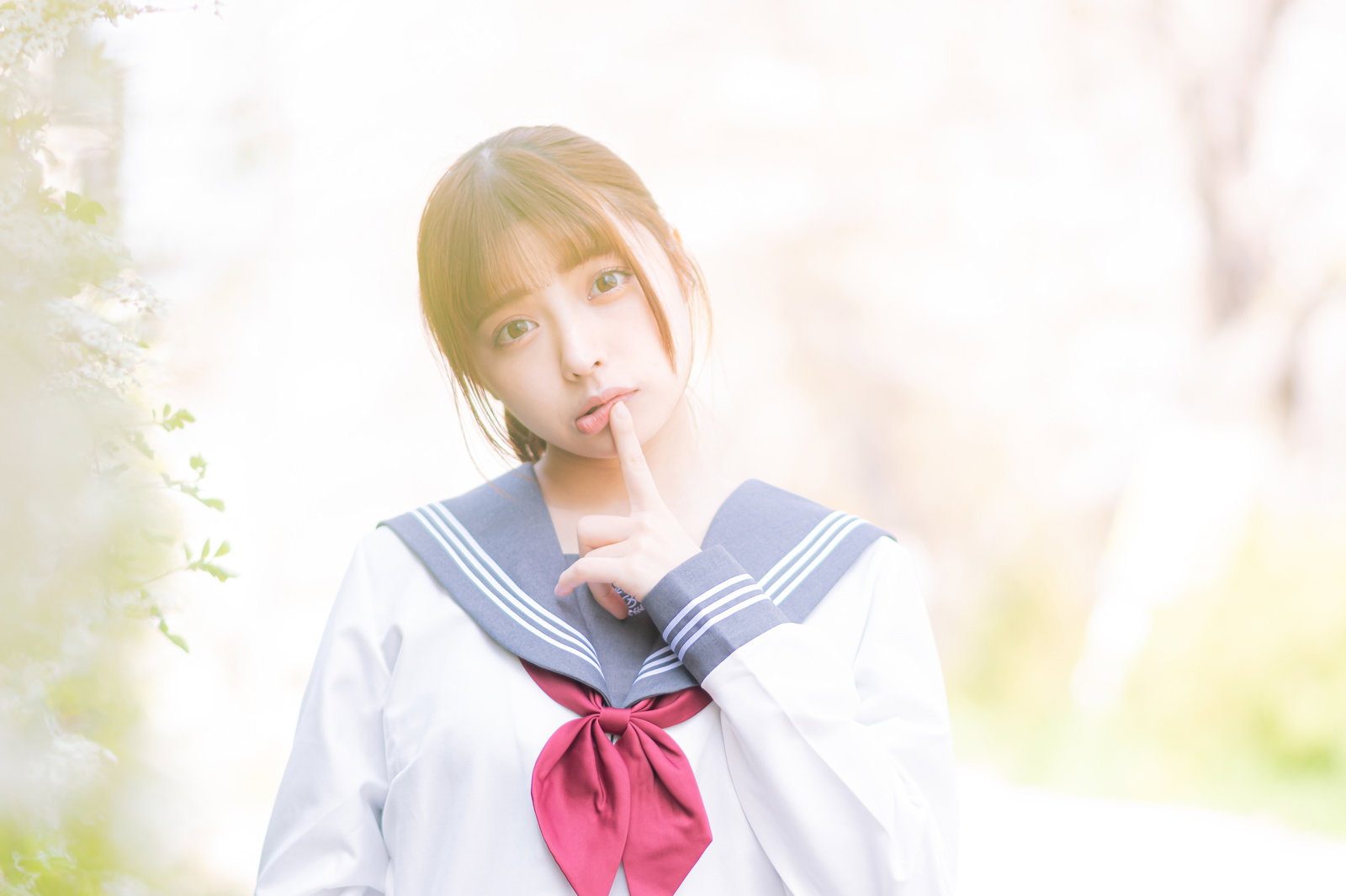 人差し指を唇に当てて上目遣いをするセーラー服姿の女子高生［モデル：高尾実生］