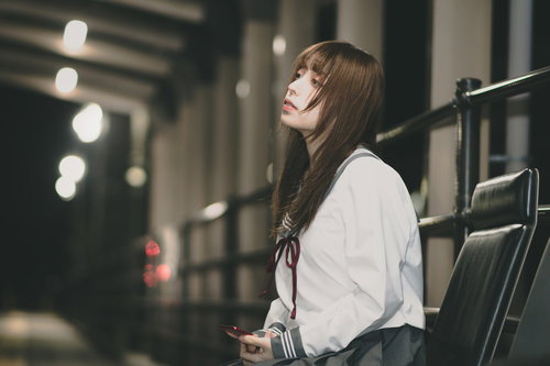 駅のホームで憂鬱な表情の女子高生、終電待ち