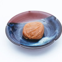 青い陶器の皿に盛られた梅干しの一粒、南高梅使用の写真