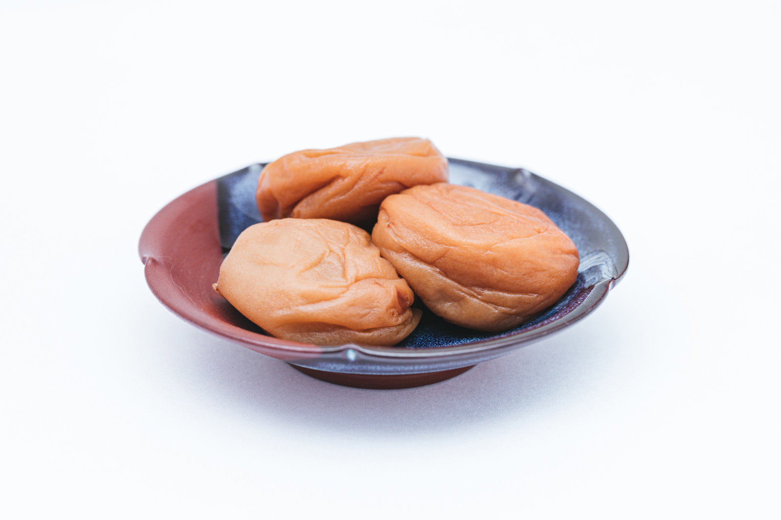 濃い紫色のお皿に赤い梅干しが数個盛られている