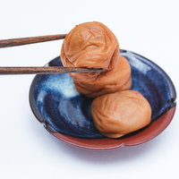 青い皿の梅干しを木製の箸で掴む和食の食事シーンの写真