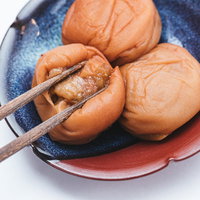 青い皿に盛られた梅干しを箸で皮から開く様子の写真