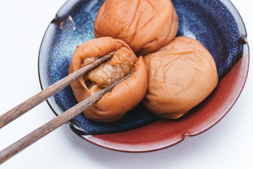 青い皿に盛られた梅干しを箸で皮から開く様子