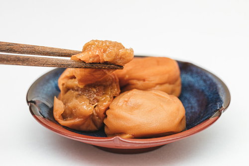 青い器の梅干しから梅肉を箸で掴む和食の食材