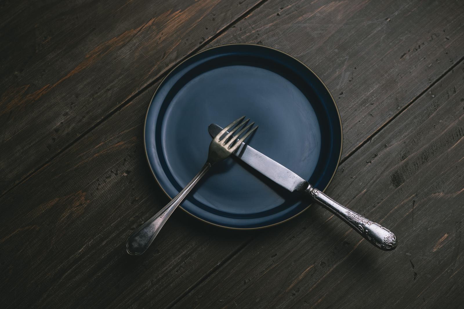 紺色の皿に置かれたナイフとフォークを重ねたテーブルマナーの食事風景