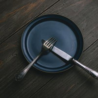 紺色の皿の上に置かれたナイフとフォークでテーブルマナーを表現の写真