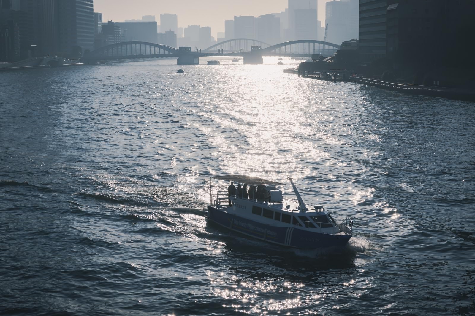 夕暮れの海を航行する急速充電型電池推進船らいちょうと背景のビル群