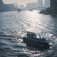 夕暮れの海を航行する急速充電型電池推進船らいちょうとビル群の写真