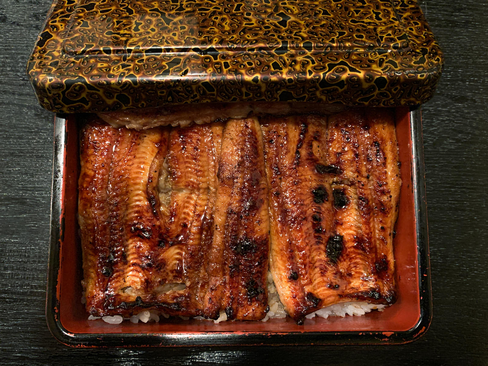 An open black lacquered box containing grilled eel on steamed rice