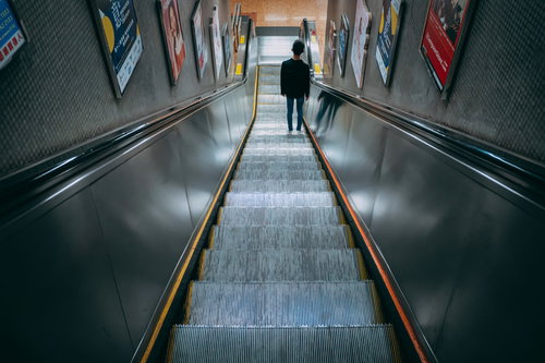 香港の地下鉄ホームへ向かうエスカレーターを降りる男性の後ろ姿