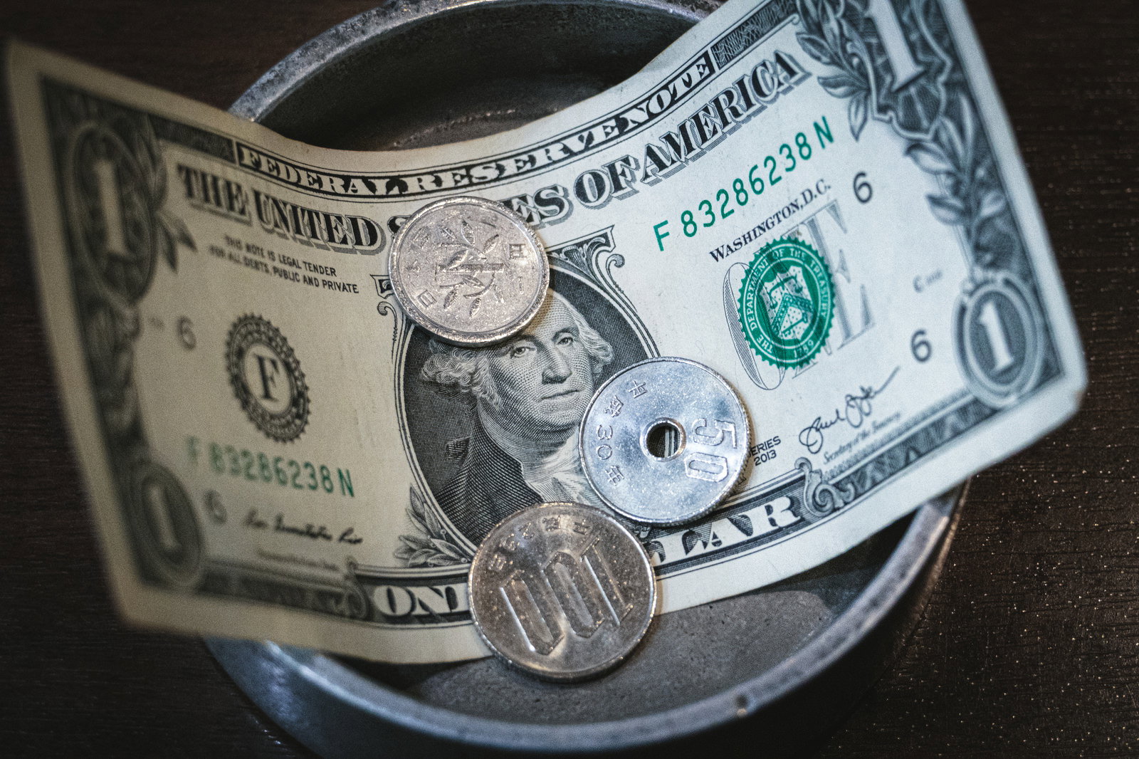 1ドル紙幣の上に100円玉、50円玉、1円玉を重ねて小皿に置いた様子