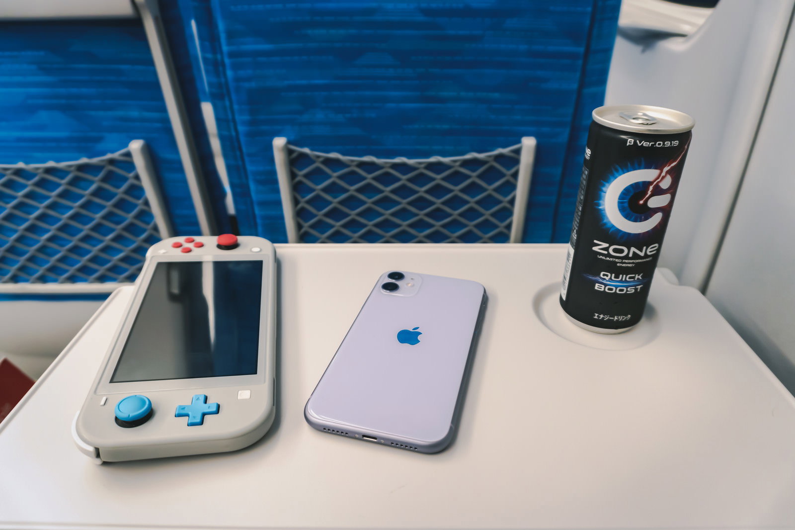 新幹線の座席テーブルにスマートフォン、ゲーム機、エナジードリンクが置かれている様子