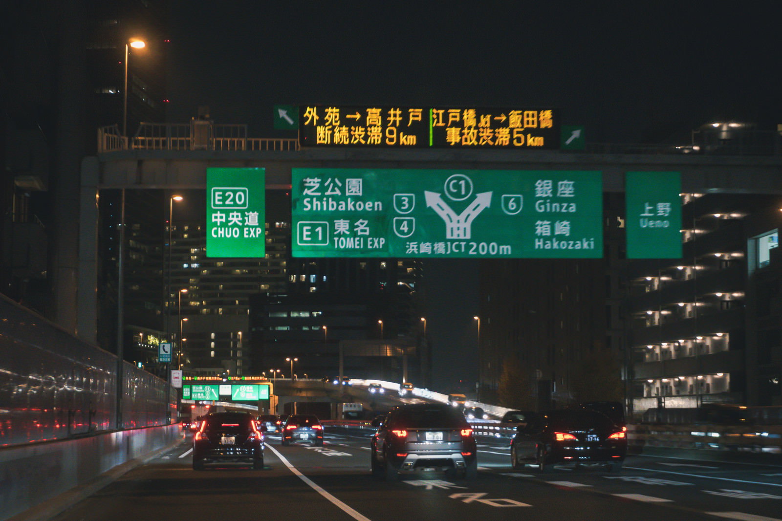 夜の高速道路で緑色の道路標識の下を走る車の列
