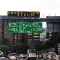 首都高速道路を走行しながら案内板を見る運転風景の写真