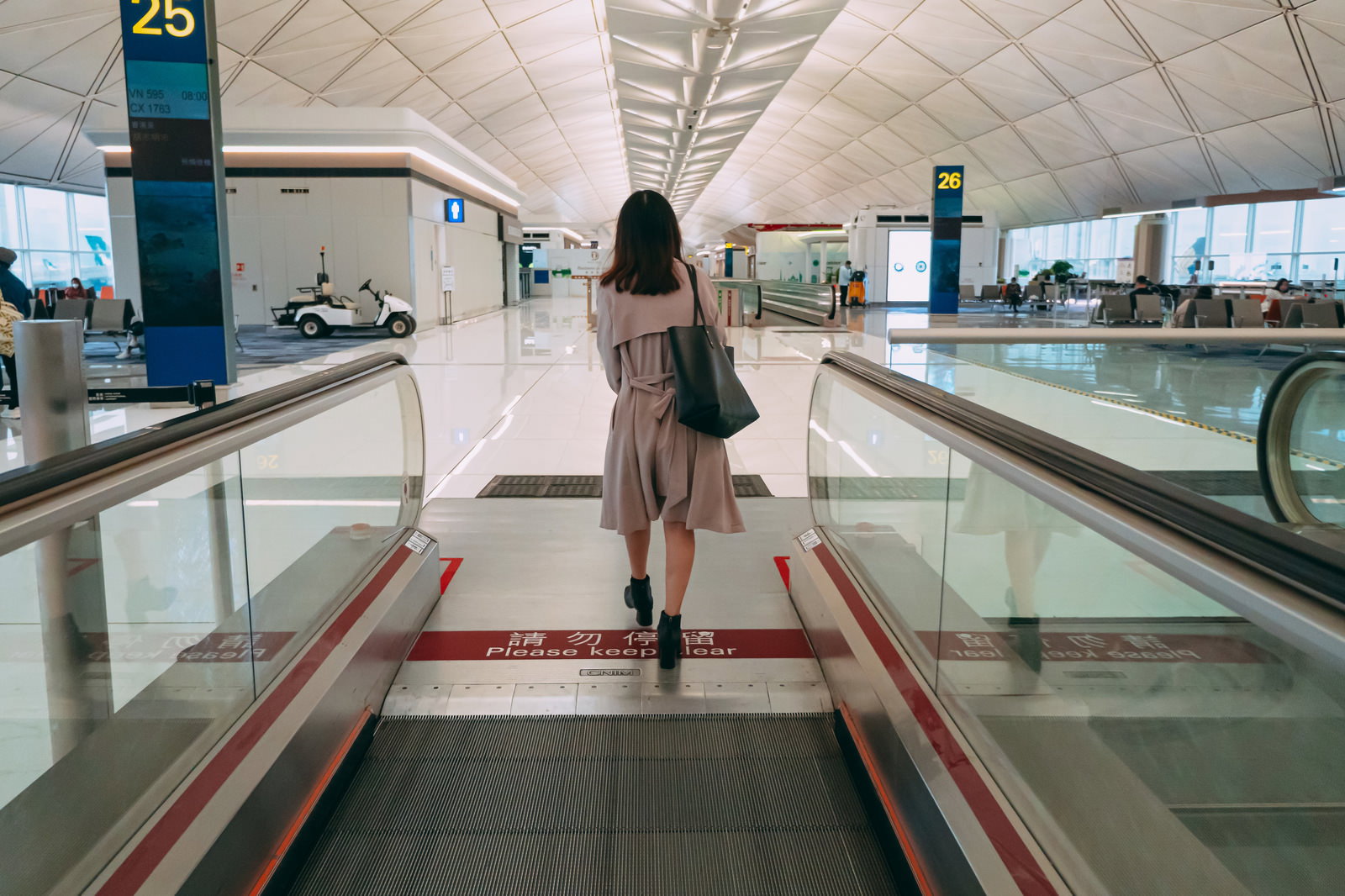 空港のターミナル内で動く歩道を歩く白い服の女性の後ろ姿