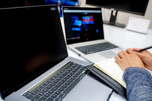 デスクにノートパソコン2台あるのにあえてメモを取る男性