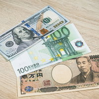 100ドル、100ユーロ、1万円の紙幣を木目のテーブルに並べた為替の写真