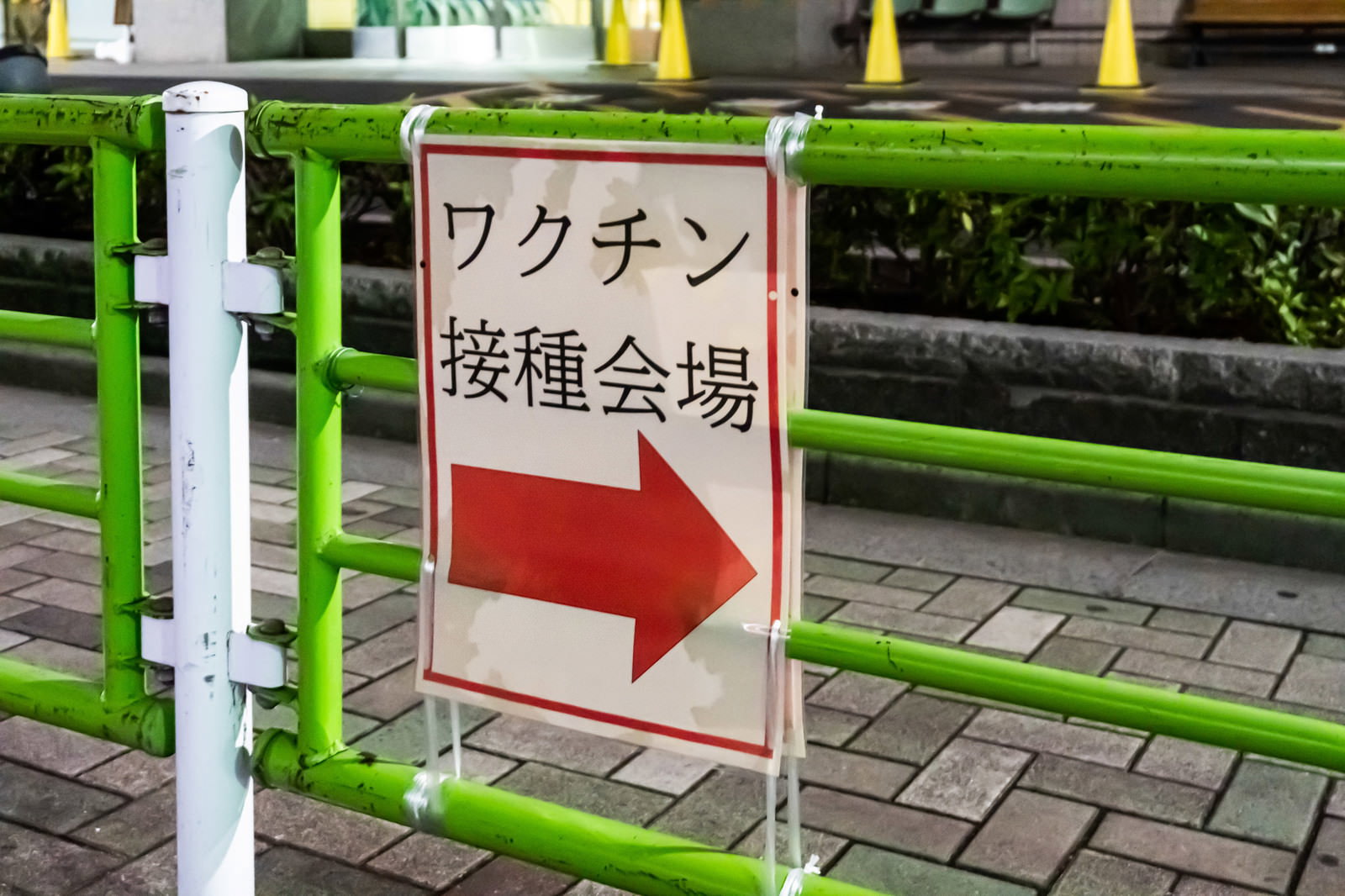 緑色のガードレールに設置された白い案内板、赤い矢印でワクチン接種会場を示している