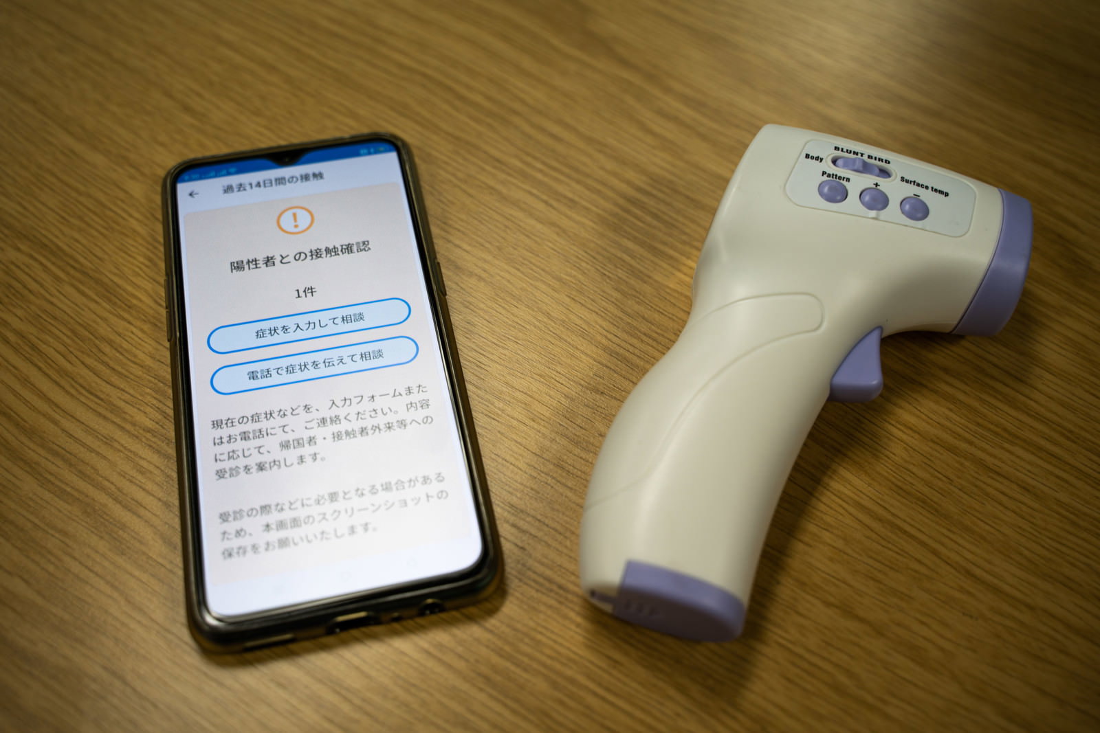 接触確認アプリの通知が表示されたスマートフォンと白い体温計
