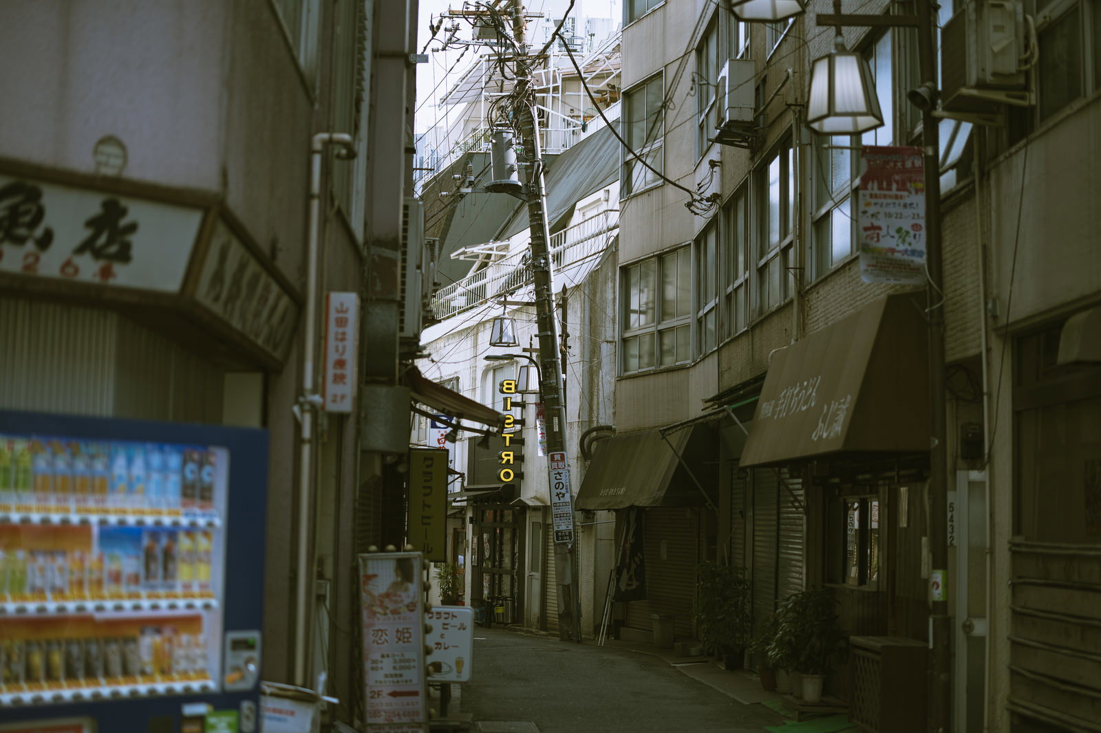 下町の路地裏で斜めに傾く電柱と電線、奥に見える建物群