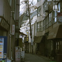 下町の路地裏に立つ斜めに傾いた電柱と古い町並みの写真