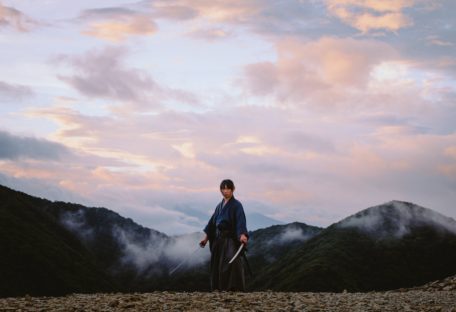 夕暮れの山中で両手に刀を構える紺色の着物の侍［モデル：まーこ］