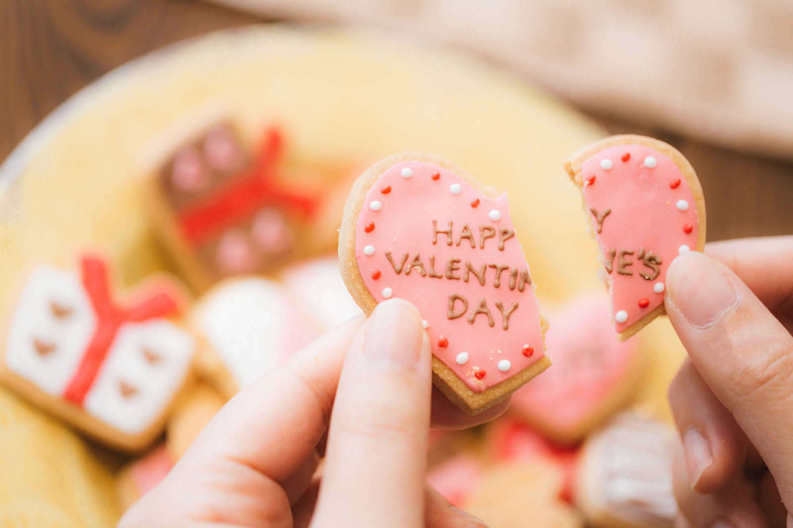 手に持たれたピンク色のハート型アイシングクッキーが真ん中から割れている様子