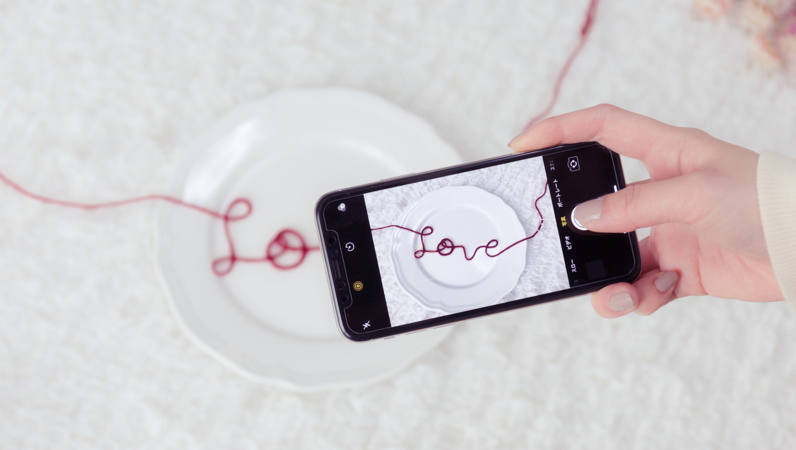 スマートフォンで赤い糸のLOVE文字を撮影する手