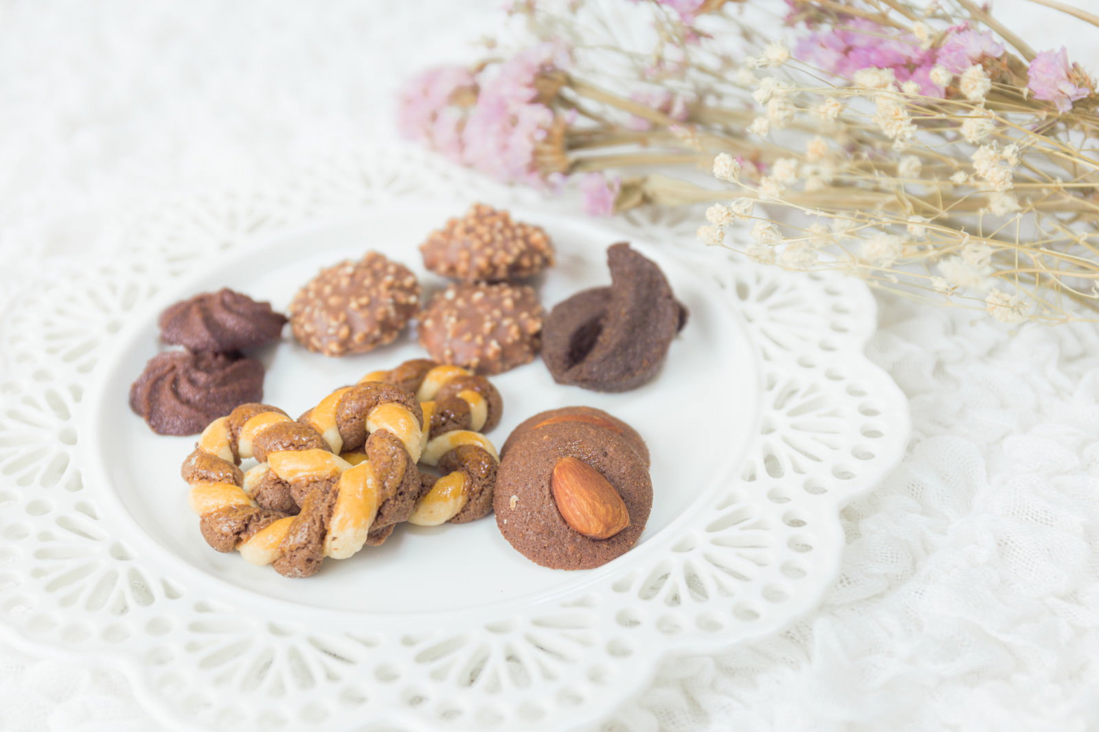 白いレース模様の皿に盛り付けられた様々なクッキーとお菓子