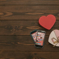 木製テーブルの上に並ぶスマートフォンとハート型のギフトボックスの写真