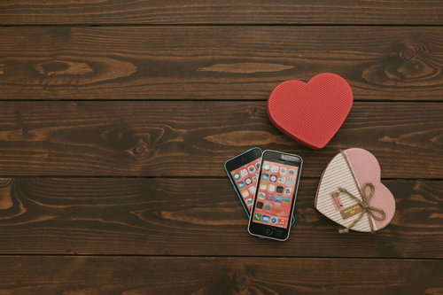 木製テーブルの上に並ぶスマートフォンとハート型のギフトボックス