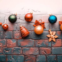 レンガ壁に並ぶクリスマスオーナメントと松の枝飾りの写真