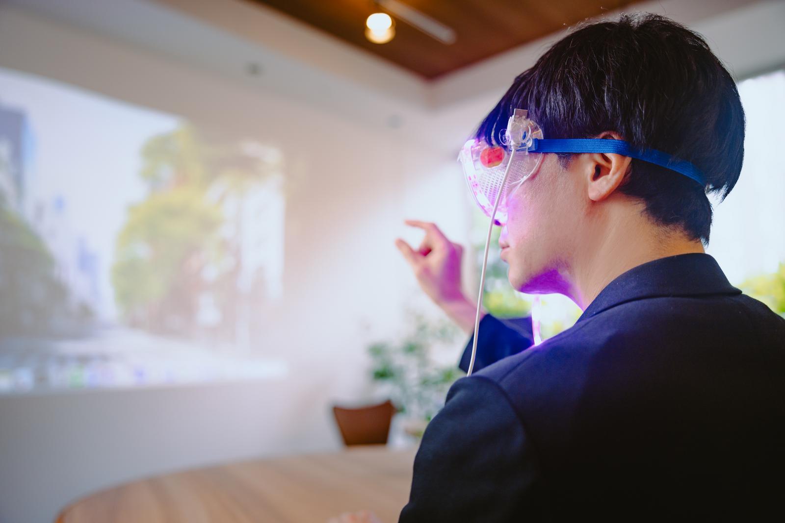 青いARゴーグルを装着して両手でジェスチャーをする黒いシャツの男性［モデル：金子周平］