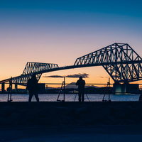 若洲海浜公園からゲートブリッジと夕焼けを撮影するフォトグラファーたちのシルエットの写真