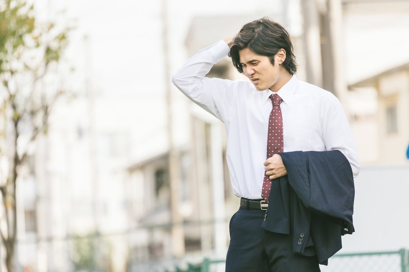ワキの臭いを気にして頭を押さえるスーツ姿の男性。都市背景［モデル：竹田匡宏］