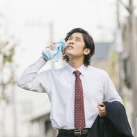 猛暑の中、飛び込み営業中の新卒男性がペットボトルで水分補給の写真