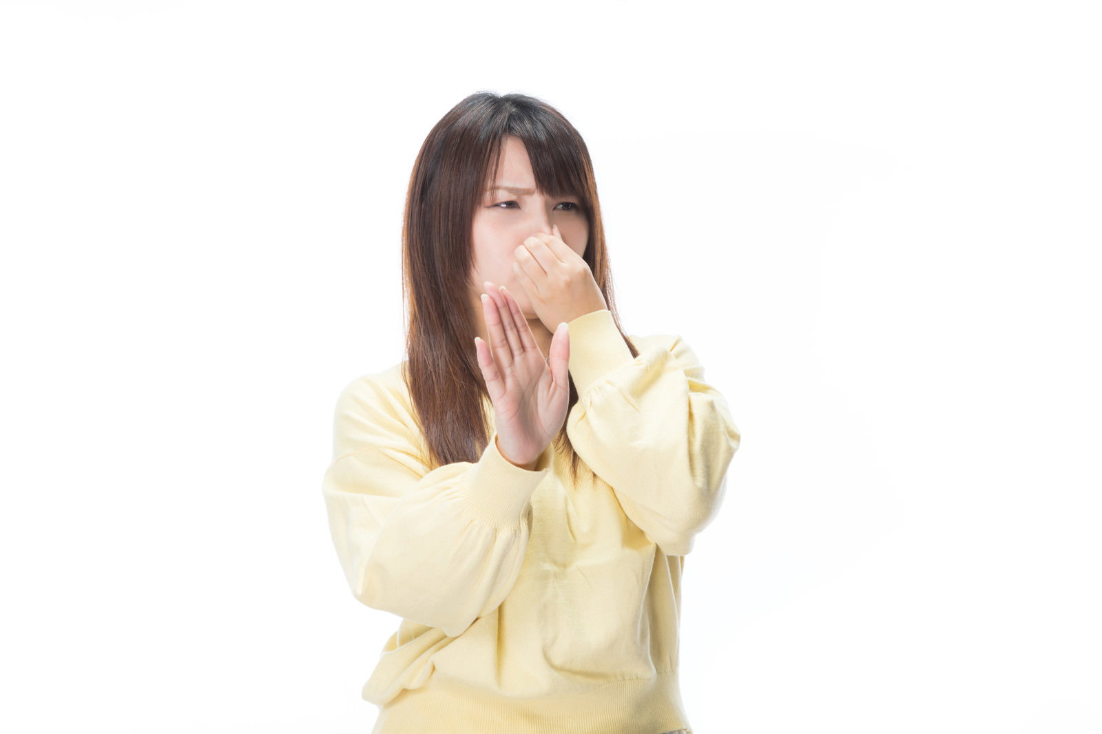 黄色い服を着た女性が両手で鼻をつまんで嫌がっている様子［モデル：Lala］
