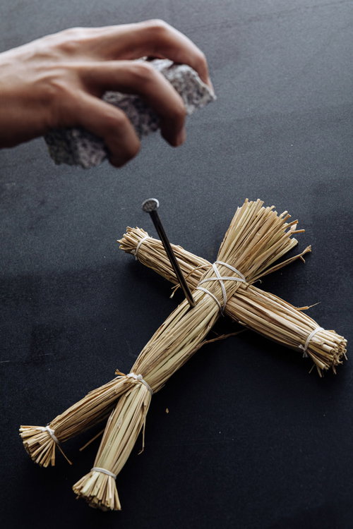 五寸釘に刺さった藁人形を石で叩く呪術の儀式