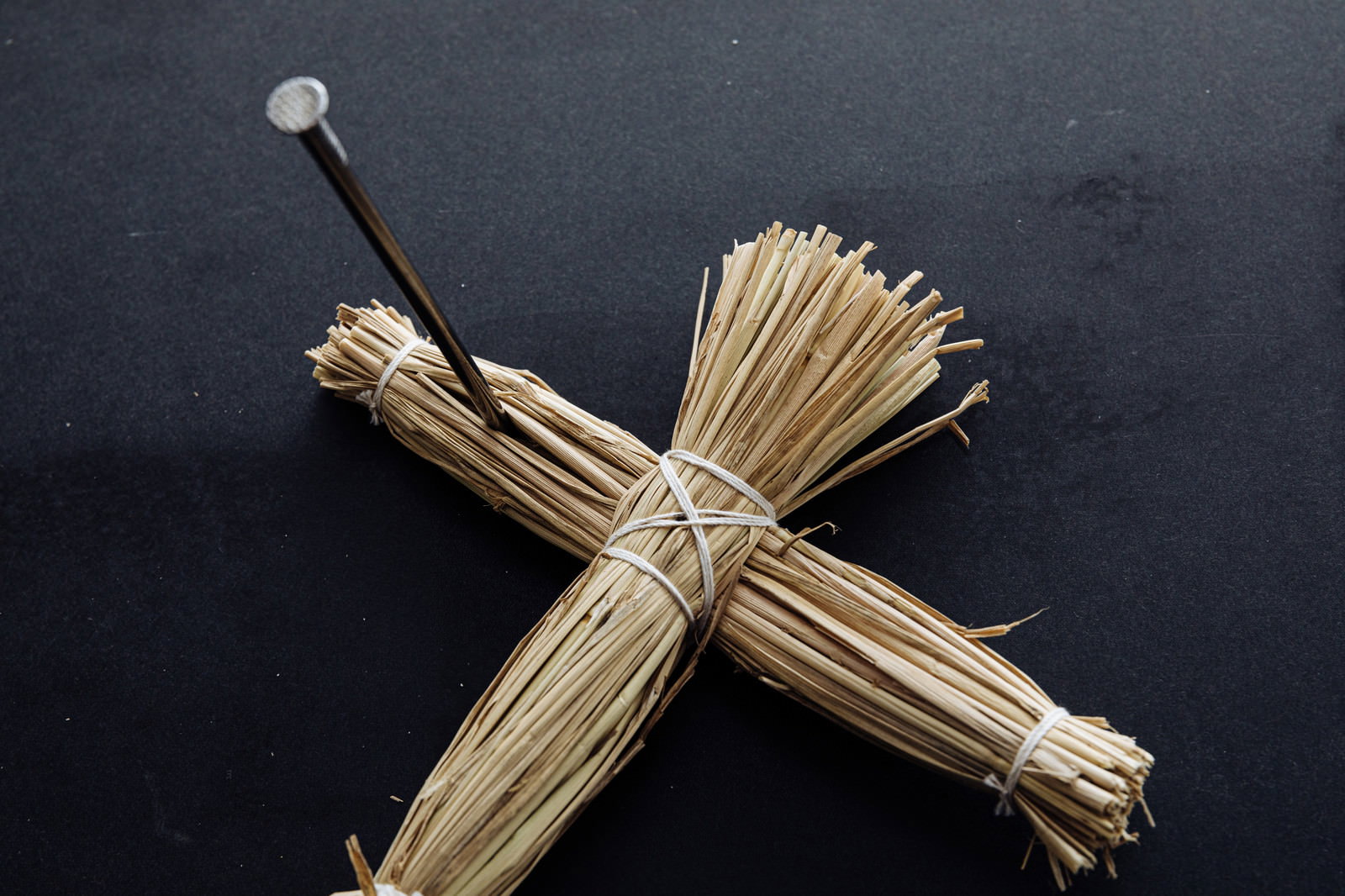 黒い背景の上に置かれた藁人形の右腕に五寸釘が刺さっている